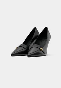 Pantofi cu toc înalt, negri, cu vârful ascuțit și un finisaj lucios din patent, având o curea încrucișată cu un accent auriu în față. Design cu toc în wedge.