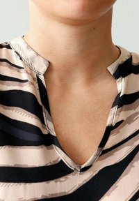 Nahaufnahme des Nackens und des Schlüsselbeins einer Person, die eine beige und schwarze gestreifte V-Ausschnitt-Bluse mit einem gezackten Kragen trägt.