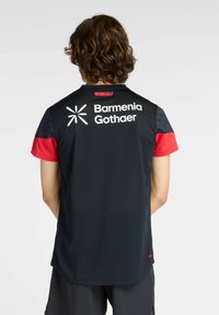 Camiseta deportiva negra con mangas cortas rojas. Presenta el logo "Barmenia Gothaer" y "WERKSELF" en la espalda. Hecha de tejido transpirable.