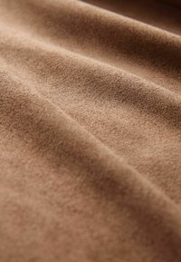 Hnědá semišová tkanina s jemnou strukturou, zdobená záhyby a hladkým povrchem. Detailní záběr, který zdůrazňuje barvu a materiálové detaily.