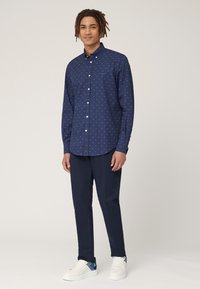 Marineblauwe overhem shirt met kleine roze patronen, lange mouwen en een kraag, gecombineerd met marineblauwe broek en witte sneakers met blauwe accenten.