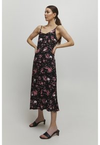 Rochie maxi neagră cu flori roz și albe, cu bretele subțiri ajustabile și tiv ondulat. Asortată cu pantofi cu toc negri, ușor de purtat.