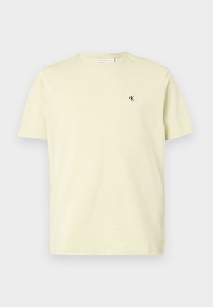 Hele beež lühikeste varrukatega ümmarguse kaelusega T-särk, mille vasakul rinnal on väike must "cK" logo, esitatud lihtsa tausta ees.