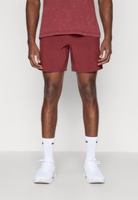 Bordeauxrode shorts van lichtgewicht stof, met een eenvoudig ontwerp, tot halverwege de dijen, gecombineerd met witte sportschoenen en sokken.