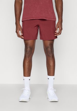 Pantalones cortos color marrón, hechos de un tejido ligero, con un diseño simple, de longitud hasta la mitad del muslo, combinados con zapatillas deportivas blancas y calcetines.