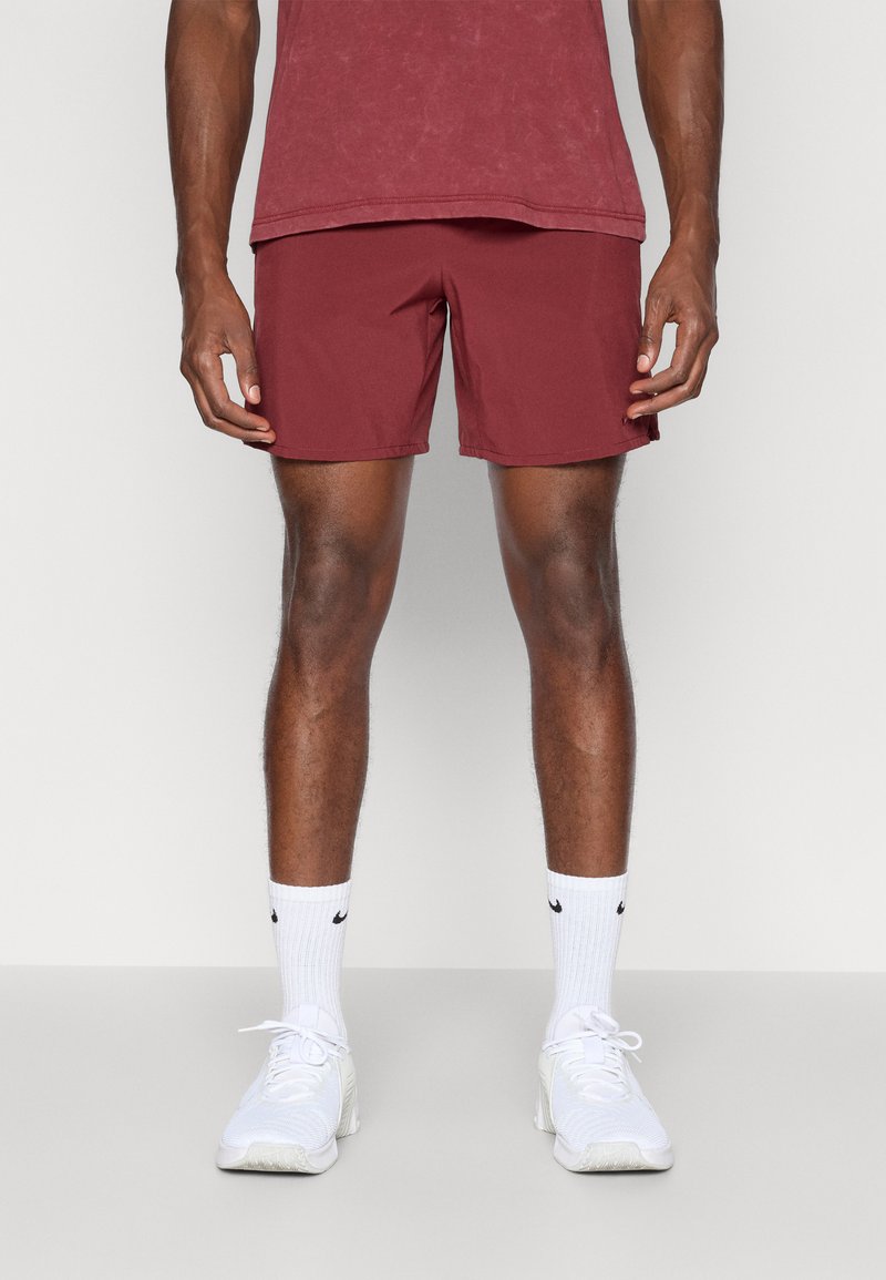 Bordeauxrode shorts van lichtgewicht stof, met een eenvoudig ontwerp, tot halverwege de dijen, gecombineerd met witte sportschoenen en sokken.