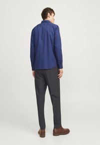 Mørkeblå skjorte med mønsterdesign, lange ermer og krage med knapper. Kombinert med mørke bukser og brune sko. Bakfra vist.