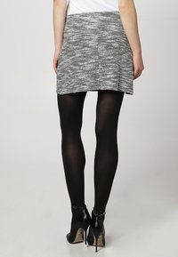 Grijze en witte textuur mini-rok met een aansluitende taille, gedragen met zwarte doorschijnende tights en zwarte hoge hakken.