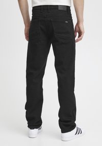 Black denim jeans with a straight cut, featuring back pockets with pointed flaps, a leather patch on the waistband, and minimal hardware accents.