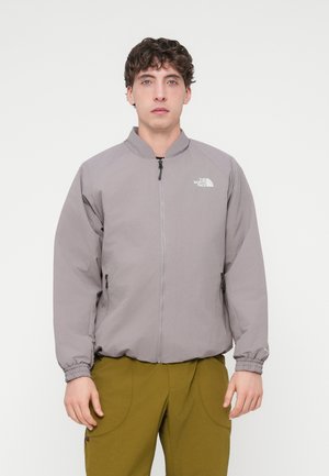 Ανοιχτό γκρι μπουφάν με φερμουάρ, γιακά σε στάση, ελαστικά μανσέτα και πλαϊνές τσέπες. Φέρει ένα μικρό λευκό λογότυπο στο αριστερό στήθος.