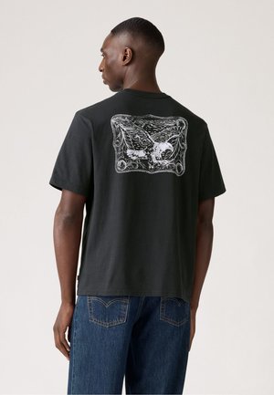 Camiseta de algodón negra con un gran gráfico blanco de un águila en la parte posterior, mangas cortas y un corte relajado.