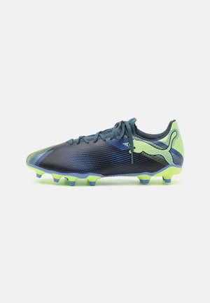 Bottes de football bleu foncé avec un motif dégradé, présentant une tige texturée, des accents néon verts et des crampons vissés pour une meilleure traction.