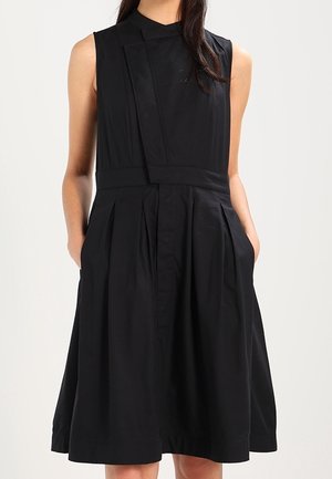 Zwarte mouwloze jurk met een hoge hals, geplooide rok, zakken en gladde stof. Heeft een gestructureerd ontwerp en strakke lijnen.