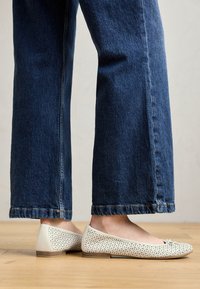 Vita perforerade ballerinaskor med rund tå, mjuk textur och platt sula, kombinerat med vida blå denimjeans.