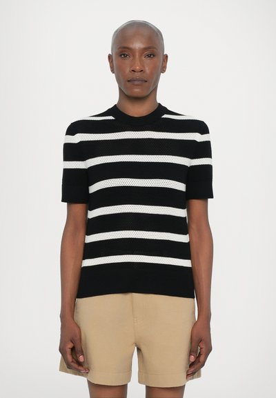 Schwarz-weiß gestreifte, gestrickte kurzärmelige Bluse mit rundem Ausschnitt und strukturiertem Finish, kombiniert mit beigen Shorts.