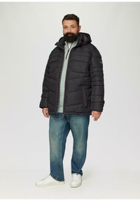 Schwarze gepolsterte Jacke mit Kapuze, zwei Brusttaschen, roten Reißverschlussdetails, über einem hellgrünen Oberteil getragen, kombiniert mit blauen Jeans und weißen Sneakers.