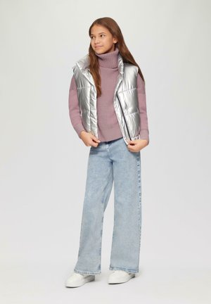 Gilet en argent sur un col roulé violet clair, associé à un jean bleu clair à jambes larges et des baskets blanches. Texture lisse et brillante.