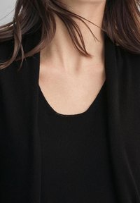 Svart stickad topp med rundad halsringning, med fina sömdetaljer och mjuk textur. Materialet verkar lätt och bekvämt.