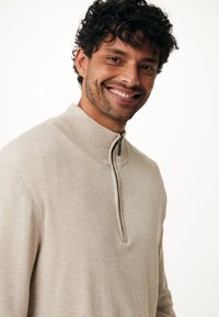 Pullover beige con colletto alto, caratterizzato da una zip frontale e un collo a costine. Texture morbida, vestibilità slim e design minimale.