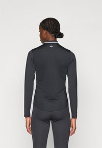 Melna sporta krekls ar garām piedurknēm un ribotu tekstūru, ar baltu akcentu apkakli un logo aizmugurē. Piegriezums izslēdz.