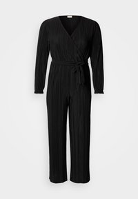 Juoda klostuota kombinezonas su ilgomis rankovėmis, V formos iškirpte ir juosmens raišteliu. Pagamintas iš tekstūruotos medžiagos, su plačiomis, trumpesnėmis kelnėmis.