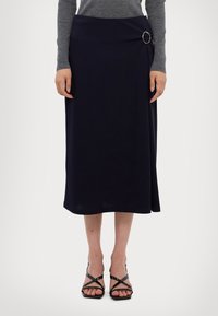 Navy midi skirt in soft fabric with an asymmetrical fold and a silver ring accent on the waist. Paired with black strappy heels.