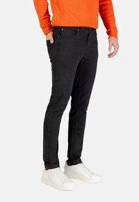 Vaqueros negros de mezclilla con un corte ajustado, que cuentan con bolsillos y detalles sutiles de costura, combinados con zapatillas blancas. La tela es suave y elástica.