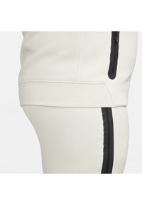 Jasnoszara bluza i dres z czarnymi paskami bocznymi, wykonane z miękkiego materiału, z zamykanymi kieszeniami na górze.