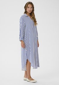 Randig skjortklänning med blå och vita vertikala ränder, krag-utförande, långa ärmar och sidslitsar; ihop med vita flats.