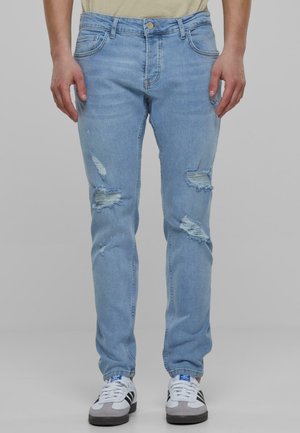 Light blue denim jeans feature multiple distressed patches, a slim fit, five-pocket style, and a button fastening at the waist.