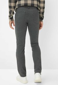 Pantaloni aderenti grigio scuro realizzati in tessuto elastico, con due tasche posteriori e una superficie liscia, abbinati a sneaker bianche.