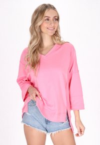 Vaaleanpunainen V-pääntie paita, jossa on kolme neljännesosaa hihat, valmistettu pehmeästä kankaasta. Yhdistetty sinisiin farkkushortseihin, joissa on rento istuvuus ja sivuhaaroja.