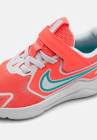 Baskets de sport en maille corail vif avec des lacets gris et une sangle Velcro. Présentent une semelle blanche et des accents turquoises sur le design.