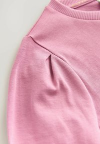 Lys pink sweatshirt lavet af blød bomuld med ribbet halsudskæring og diskret plissédetalje på skulderen, der har en tekstureret overflade.