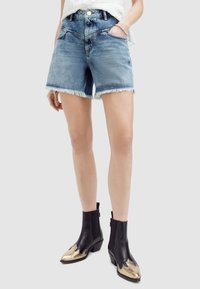 Shorts de mezclilla con dobladillo deshilachado, color azul claro, cuatro bolsillos; combinados con botines negros con detalles dorados y punteras puntiagudas.