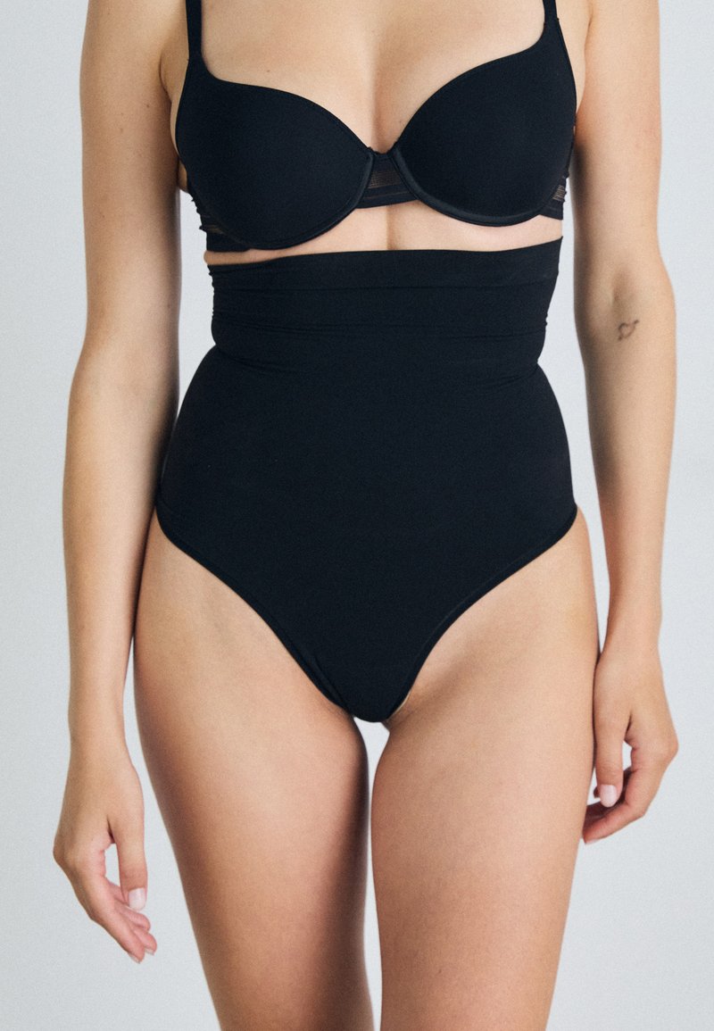 Black high-waisted swimsuit with a smooth texture, structured design, and a wide waistband for support, featuring a modest cut leg opening.