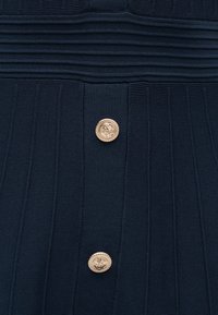 Σκούρο ναυτικό μπλε ριμπ ύφασμα με δύο χρυσά διακοσμητικά κουμπιά που φέρουν περίπλο κα ανάγλυφα σχέδια.