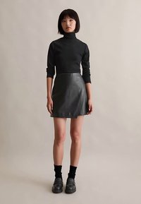 Maglione a collo alto nero abbinato a una minigonna in pelle nera con design avvolgente, completato da scarpe nere robuste e calzini.