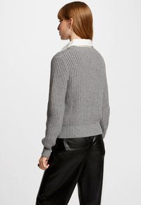 Pull en maille grise avec un motif texturé, manches et ourlet côtelés, associé à un pantalon en cuir noir. Présenté vue de dos.