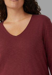 Burgunderfarbene V-Ausschnitt Langarmbluse aus weichem, strukturiertem Stoff, mit komfortablem Schnitt und subtilen, tonal variierenden Farben.