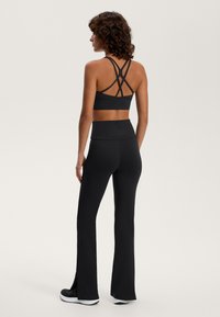 Črn športni set, ki vključuje športni modrček s prečnimi naramnicami in visokim pasom, razširjene legice z bočnimi razpoki, izdelane iz fleksibilnega blaga.