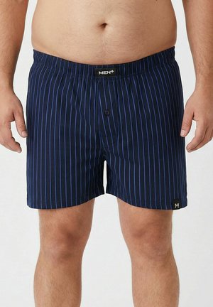 Man wearing navy blue boxer shorts with thin vertical blue stripes, elastic waistband, and front button closure.