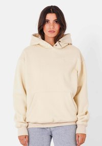 Felpa beige con cappuccio e tasca frontale, realizzata in tessuto morbido, con logo ricamato sul petto. Vestibilità rilassata e polsini a costine.