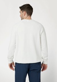 Felpa bianca con maniche lunghe raglan, polsini a coste e orlo arrotondato. Texture liscia, design semplice senza motivi o accenti visibili.