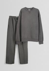Sweat-shirt gris foncé à manches longues avec poignets côtelés et pantalon de jogging assorti à taille élastique avec cordon et poches latérales, présenté sur fond gris.