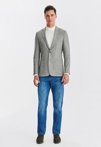 Szary żakiet w jodełkę z klapami, na jeden guzik i dwiema przednimi kieszeniami, w połączeniu z niebieskimi dżinsami i oliwkowymi butami.