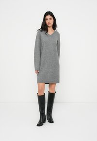 Γκρι πλεκτό φόρεμα με V-λαιμόκοψη, μακριά μανίκια και ίσια γραμμή. Φορεμένο με μαύρες μπότες έως το γόνατο. Λείες υφές και καθημερινό ύφος.