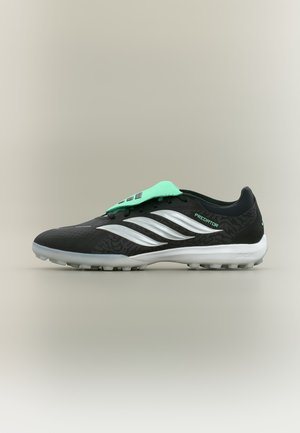 Chaussure de football Adidas Predator noire et argent avec languette vert menthe et semelle blanche à petits crampons pour gazon synthétique.