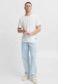 Witte katoenen T-shirt met korte mouwen, ronde hals, ontspannen pasvorm, gecombineerd met lichtblauwe jeans en beige sneakers met roomkleurige accenten.
