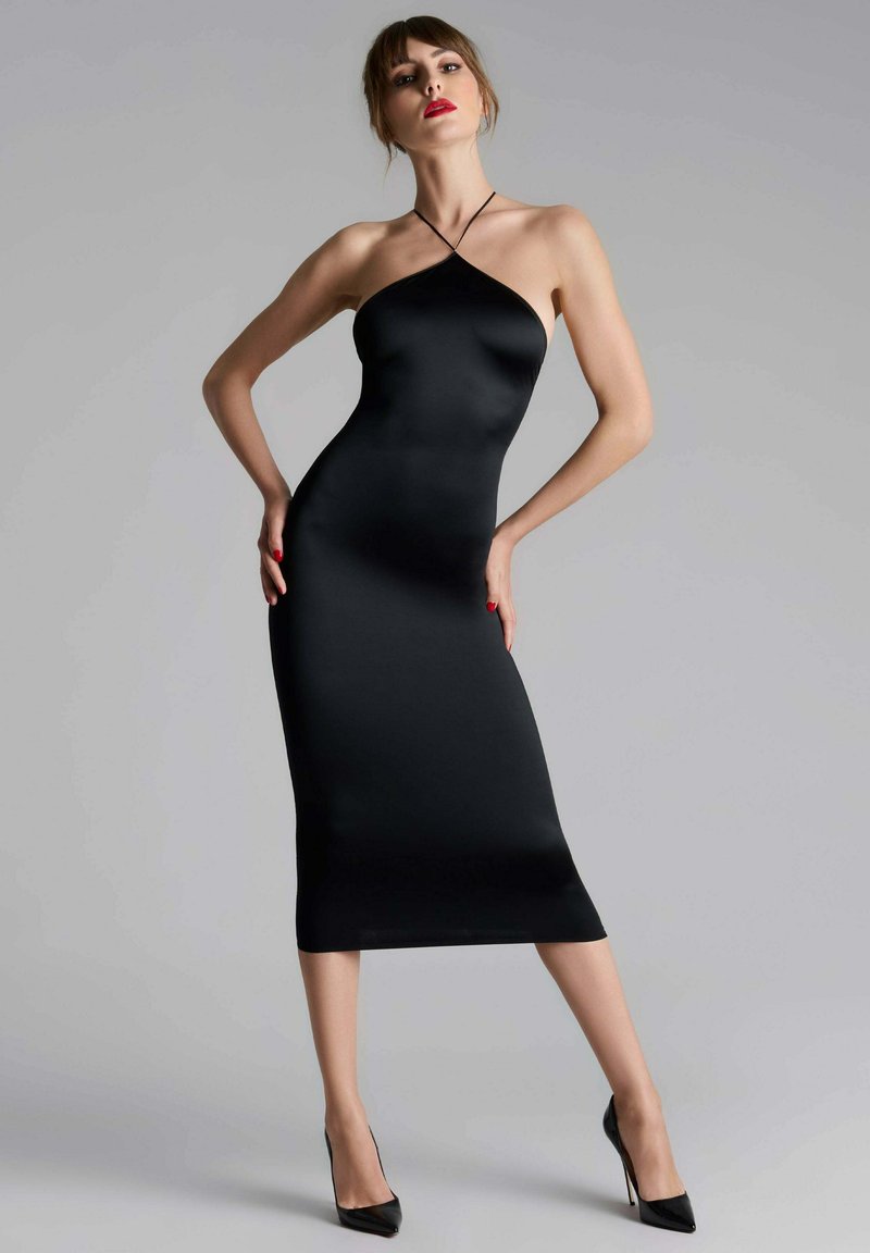 Robe noire midi avec une silhouette ajustée, un design à col halter et une texture lisse. Portée avec des escarpins noirs, sur un fond gris.